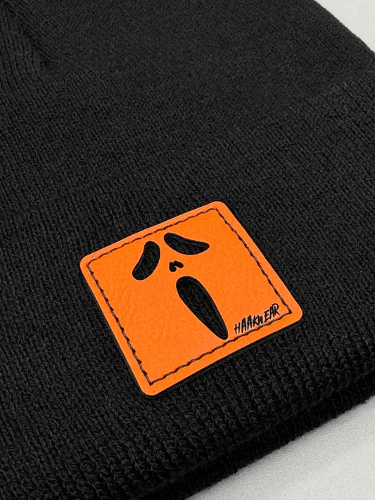 Black knit beanie detail: orange logo patch with black screaming face