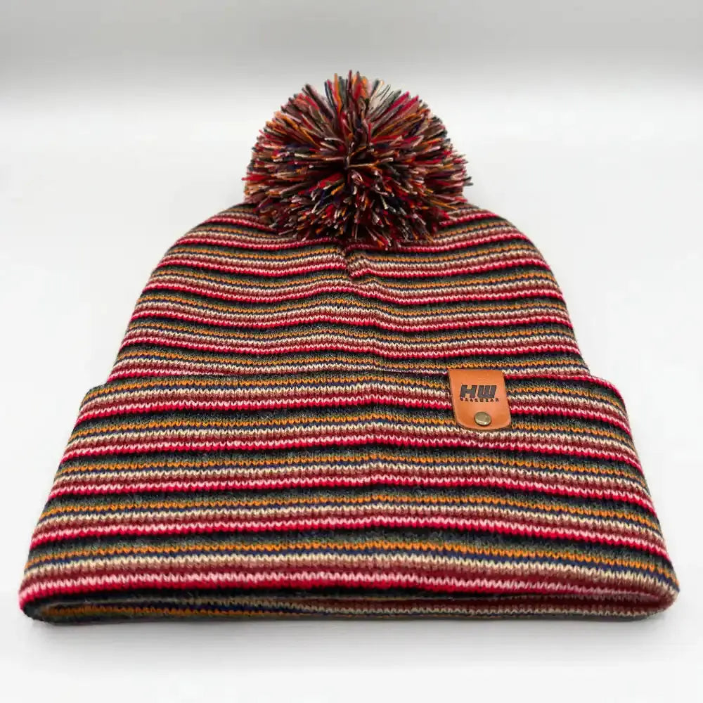 Multicolor striped knit beanie with large pom pom and tan logo patch, front view