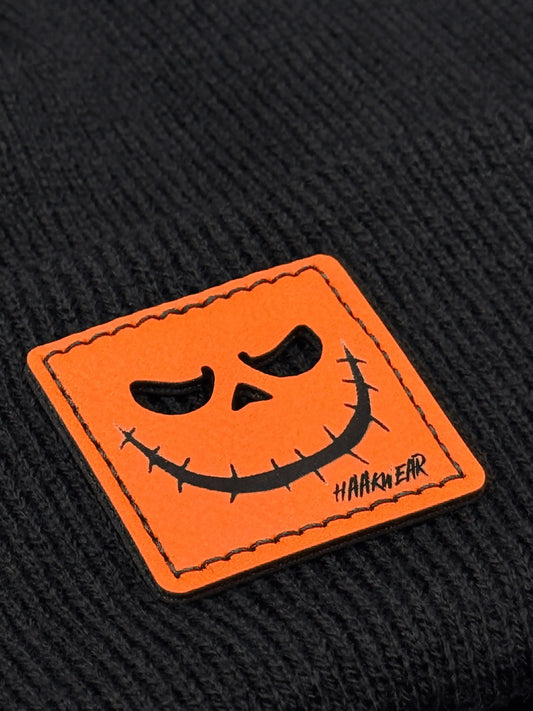 Orange jack-o-lantern face patch on dark knit beanie with stitched border