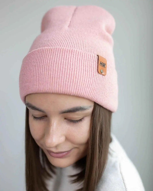 Pearl pink ribbed cuff beanie worn on head, small leather logo patch.