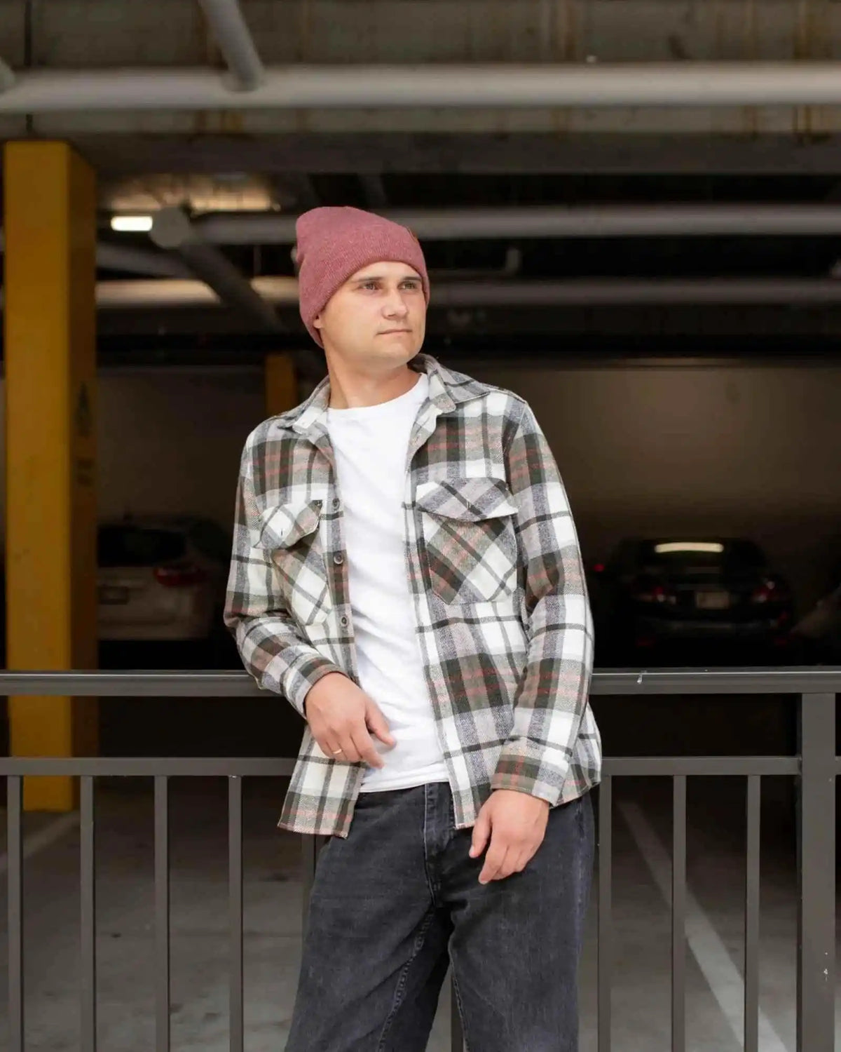 Rusty burgundy beanie with folded cuff and tan logo patch, worn with plaid overshirt.