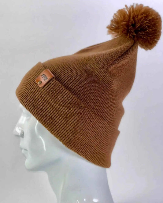 Camel brown pom pom beanie angled on mannequin head, cuffed knit with label patch