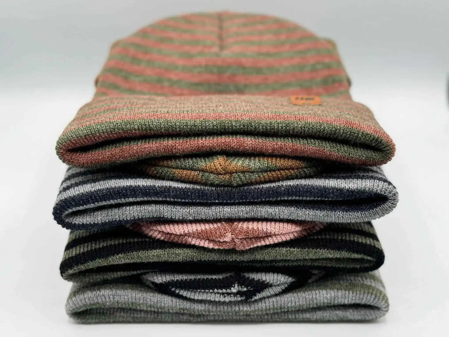 Stack of cuffed beanies showing burgundy, green, and dark stripe bands