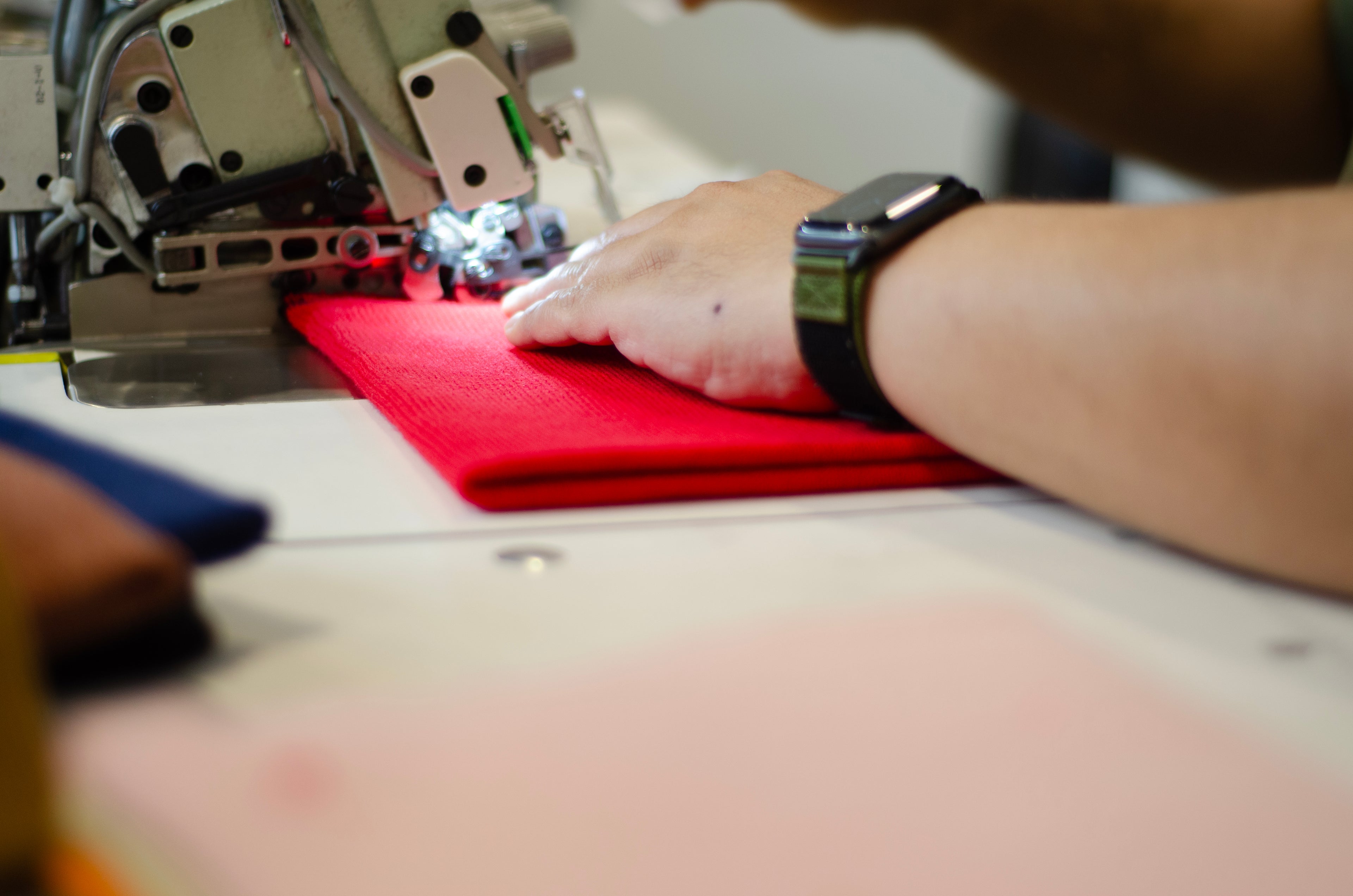 Person sewing red fabric on a machine with a blurred background