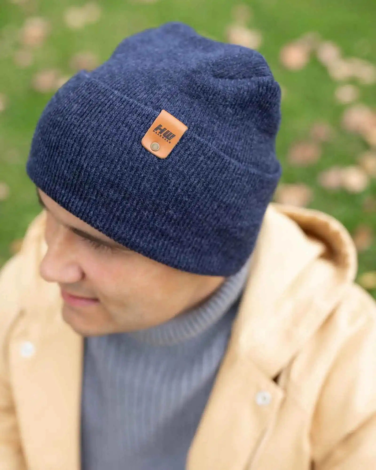Denim blue knit beanie with tan logo patch on cuff, close side view