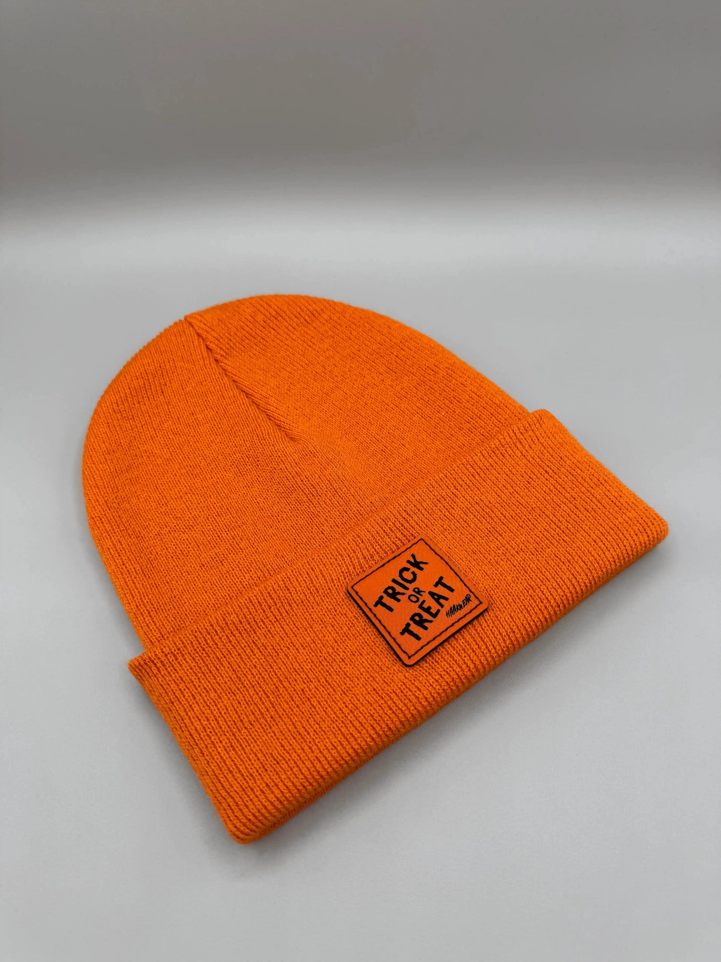 Orange beanie laid flat with square “Trick or Treat” logo patch