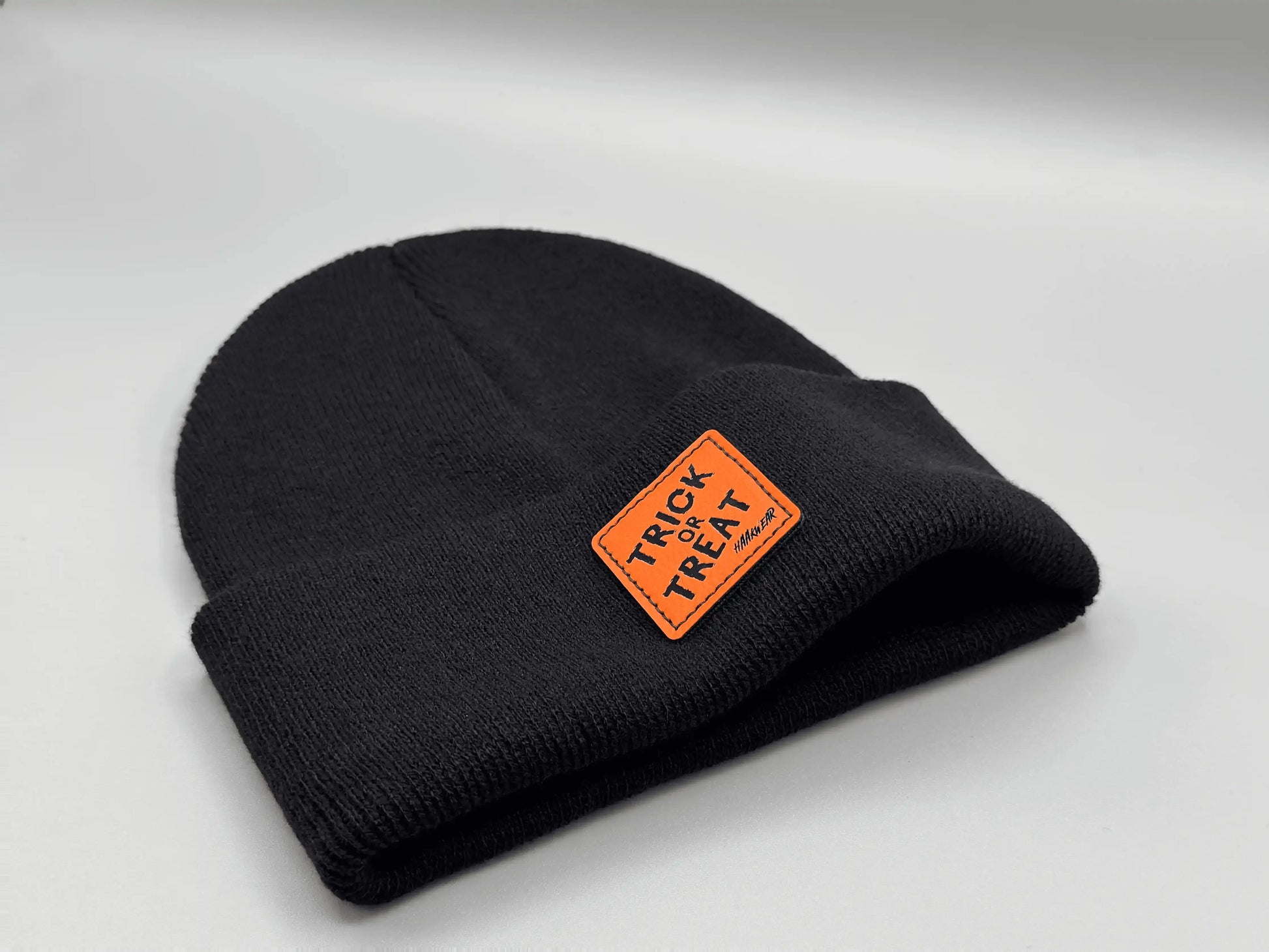 Dark beanie with orange “Trick or Treat” logo patch, side view
