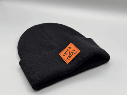 Dark beanie with orange “Trick or Treat” logo patch, side view