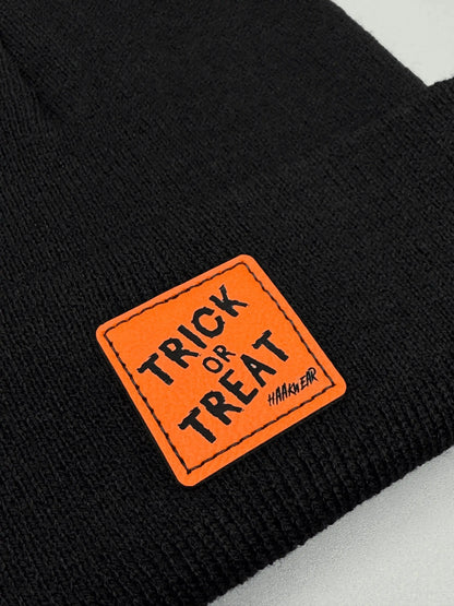 Dark knitted beanie with orange “Trick or Treat” logo patch