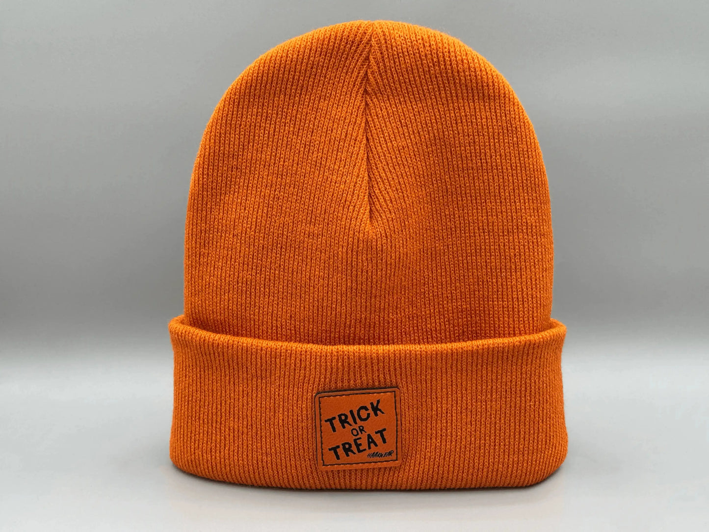 Orange knitted beanie with square “Trick or Treat” logo patch, side view