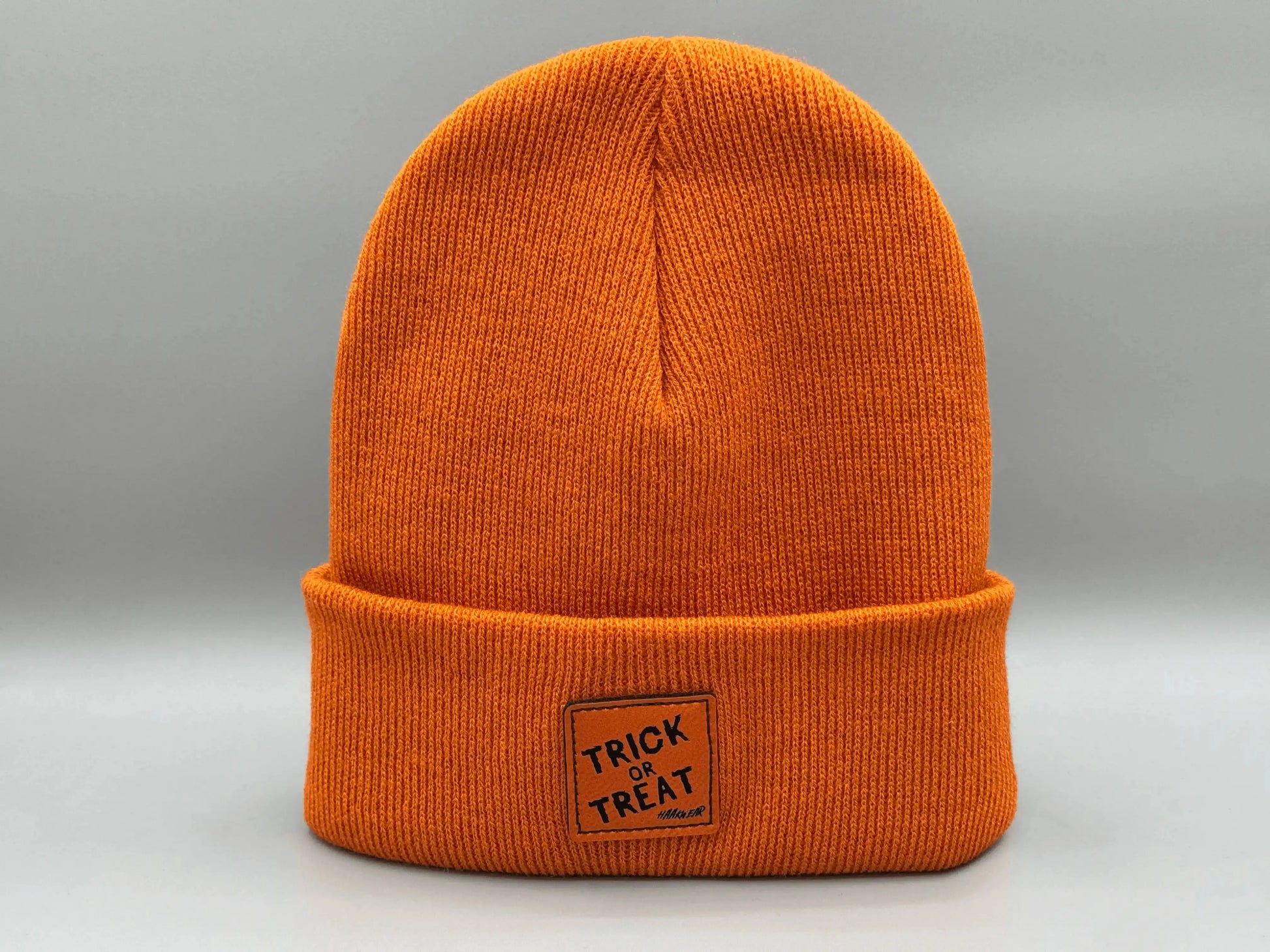 Orange knitted beanie with square “Trick or Treat” logo patch, side view