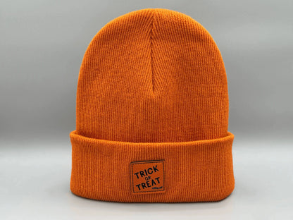 Orange knitted beanie with square “Trick or Treat” logo patch, side view