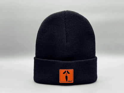Dark knit beanie with ribbed cuff and small orange rectangular character patch