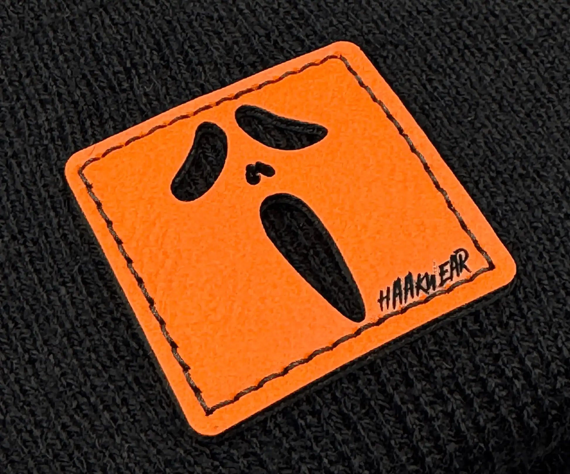 Black knit beanie close-up of orange rectangular character logo patch