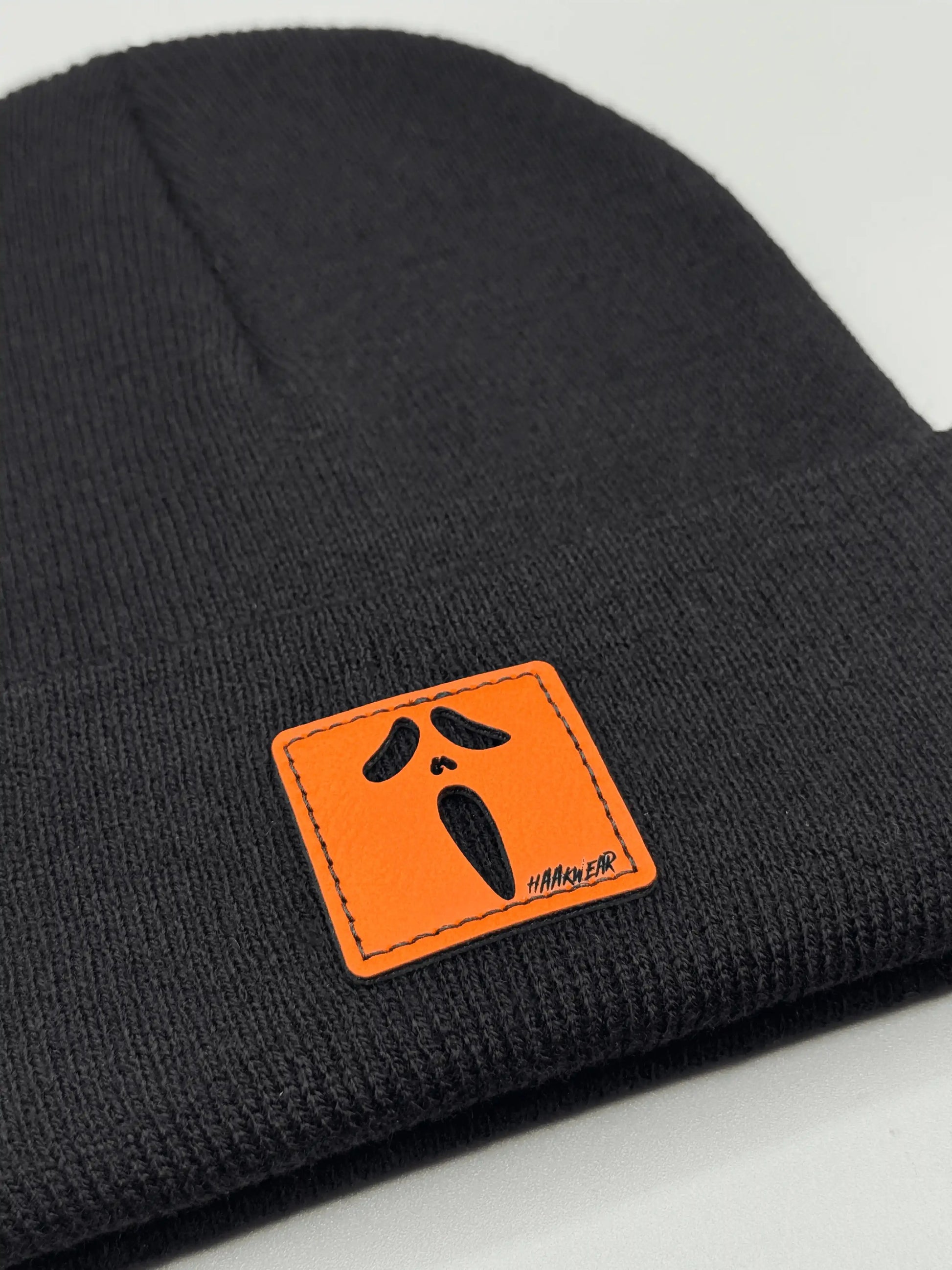 Black knit beanie with ribbed cuff and orange rectangular character patch