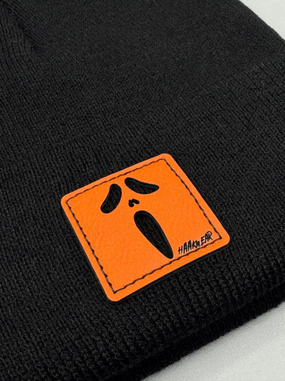 Black knit beanie detail: orange logo patch with black screaming face