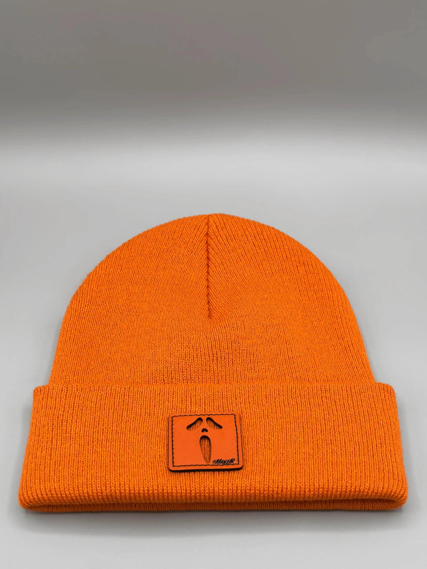Orange knit beanie with ribbed cuff and small square character patch on front
