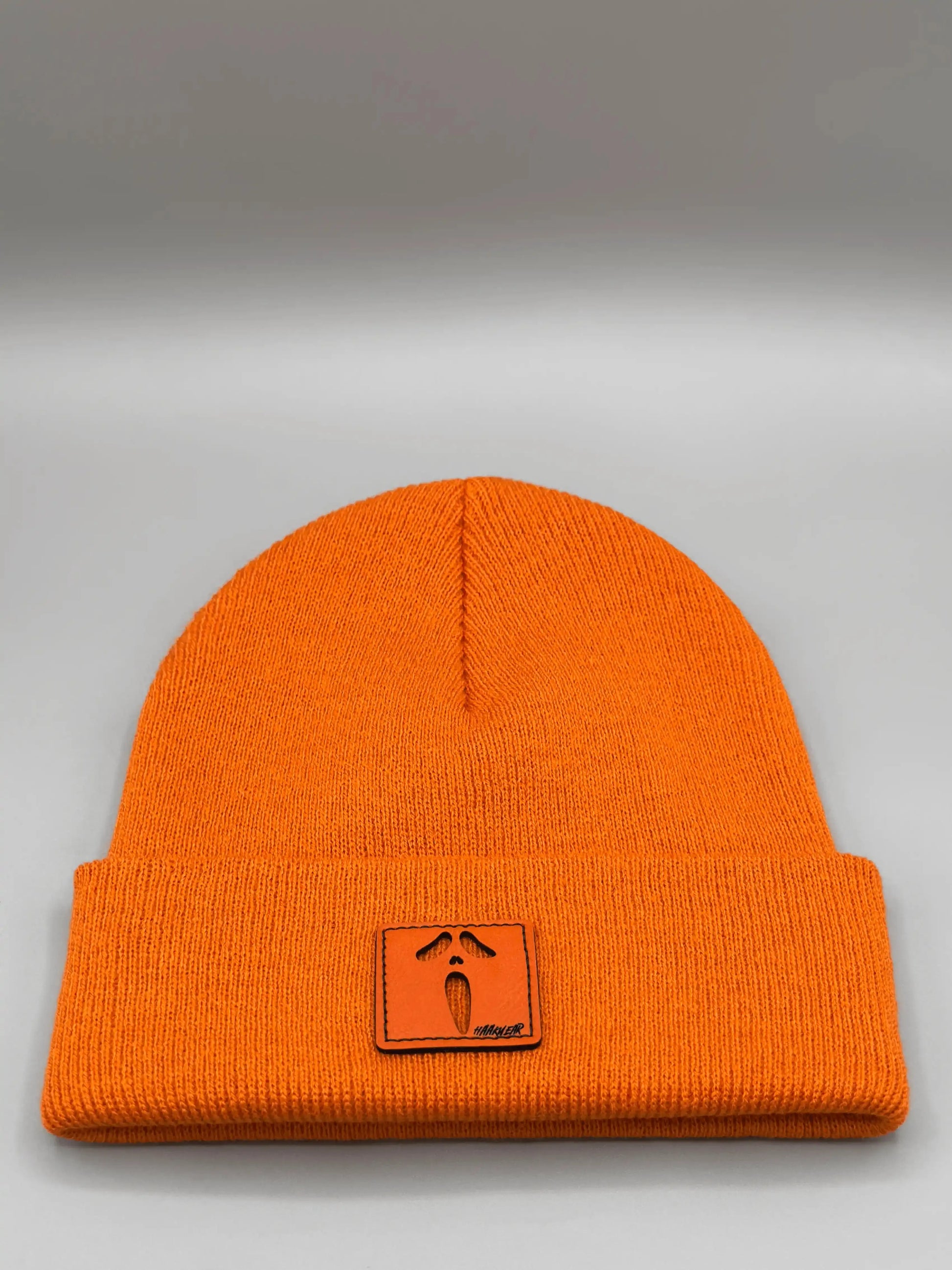 Orange knit beanie with ribbed cuff and small square character patch on front