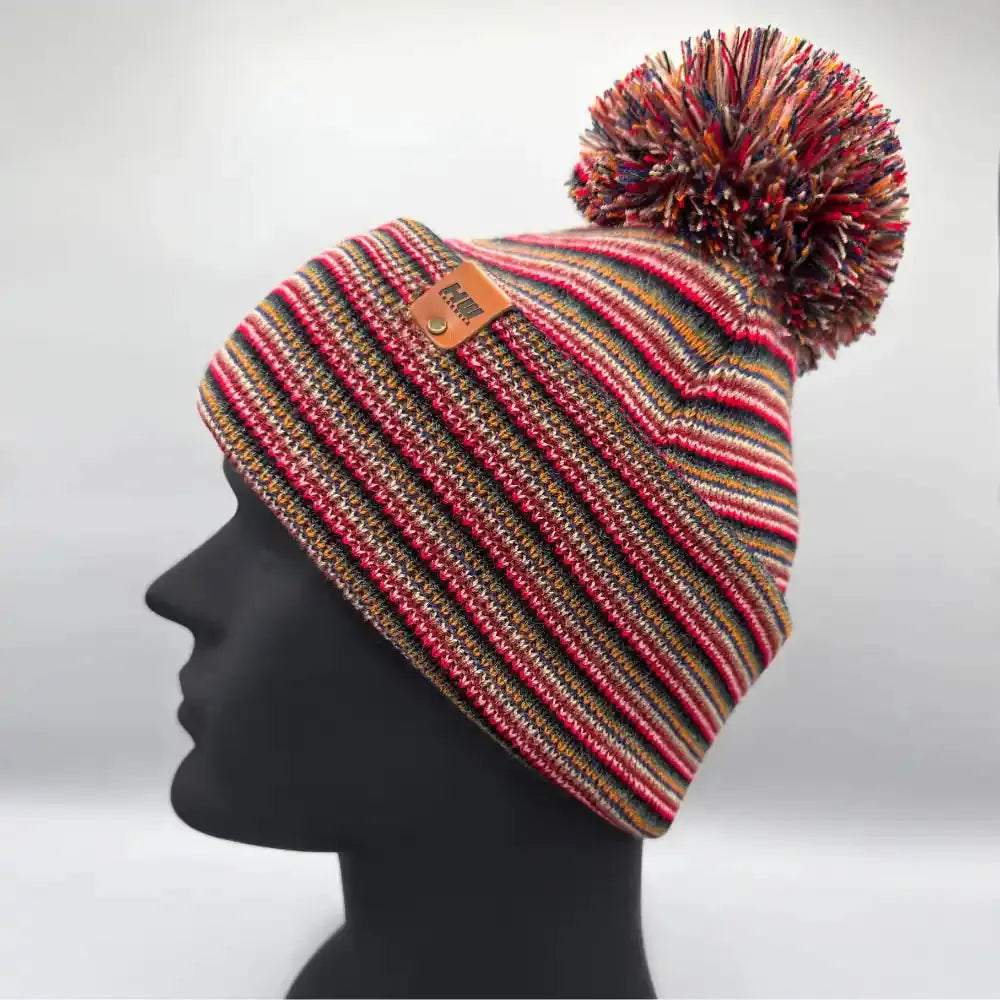 Multicolor striped beanie with large pom pom and tan leather logo patch
