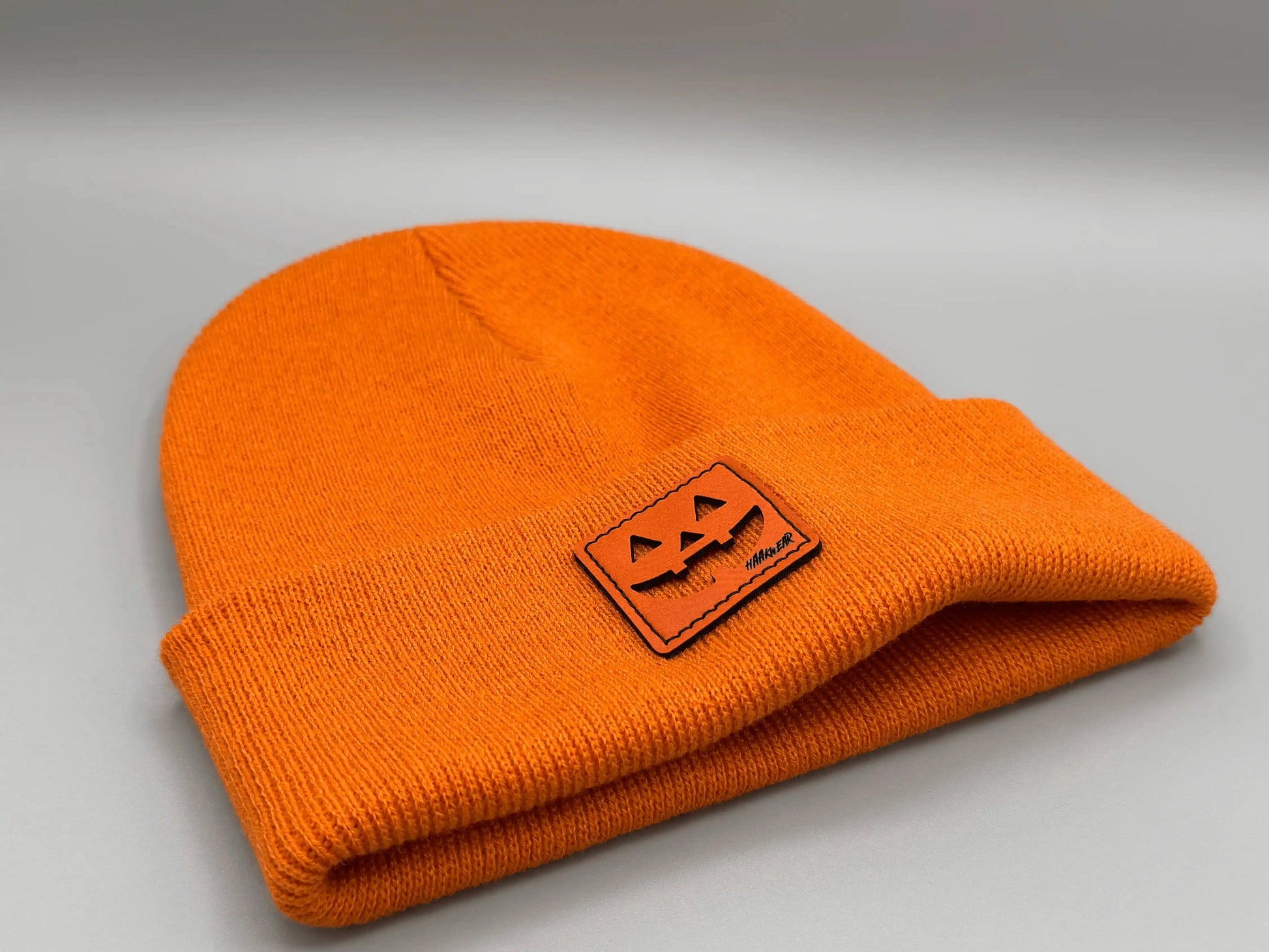 Folded orange knit beanie with jack-o-lantern logo patch near the edge