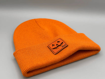 Folded orange knit beanie with jack-o-lantern logo patch near the edge