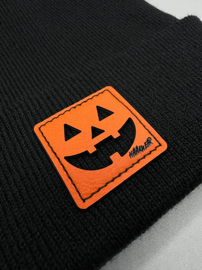 Close-up of black beanie knit with orange jack-o-lantern logo patch