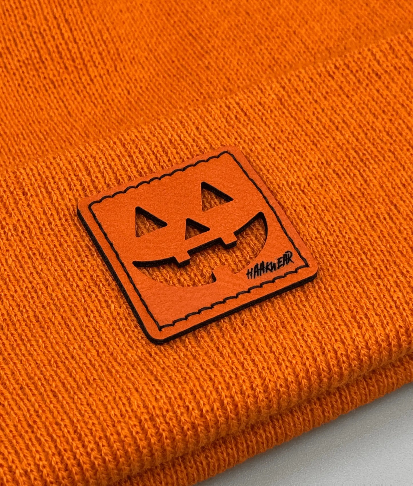 Orange knit beanie with stitched jack-o-lantern logo patch on the cuff