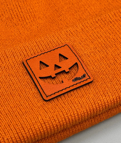 Orange knit beanie with stitched jack-o-lantern logo patch on the cuff