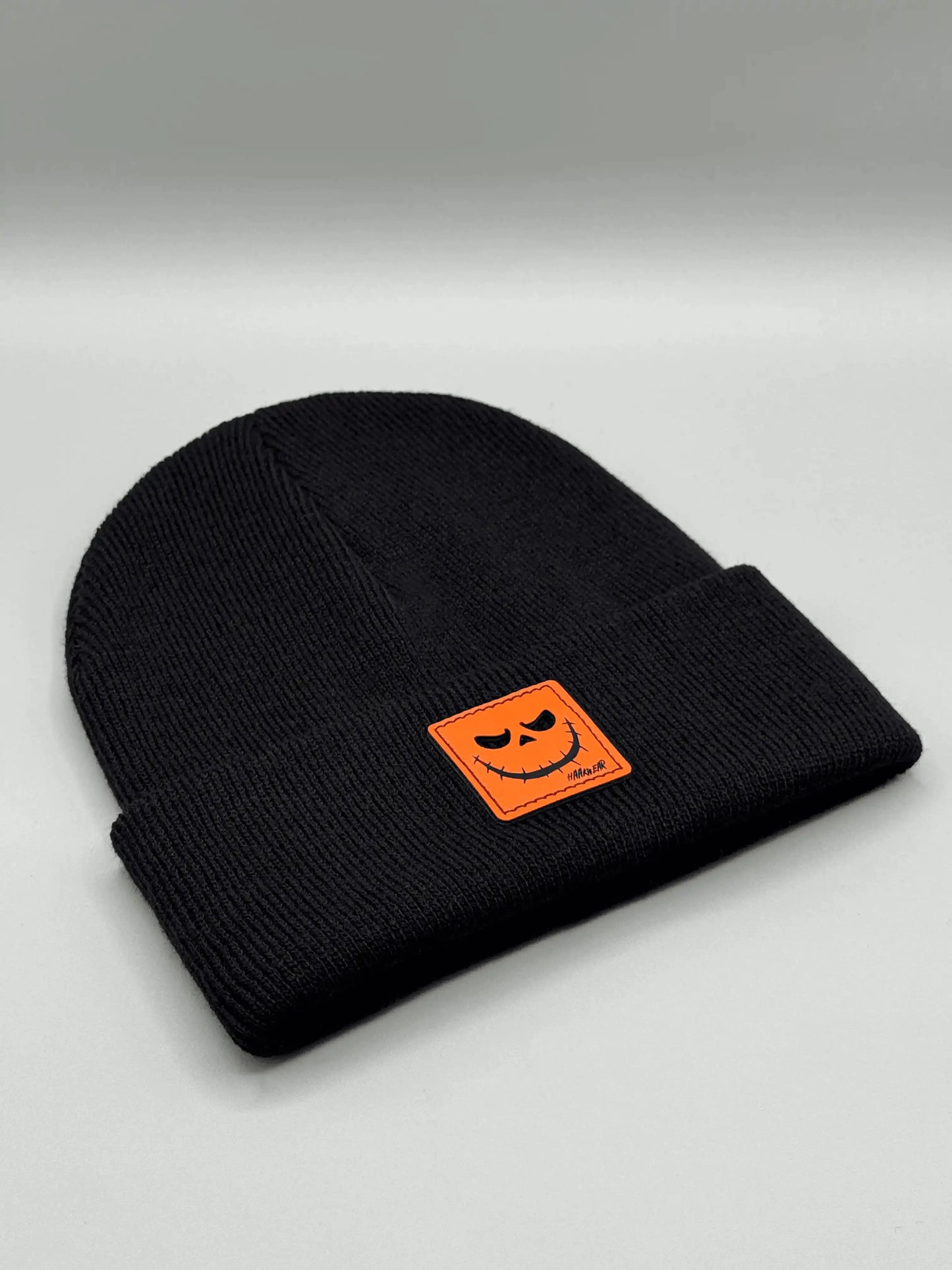 Black knit beanie with orange jack-o-lantern patch on front