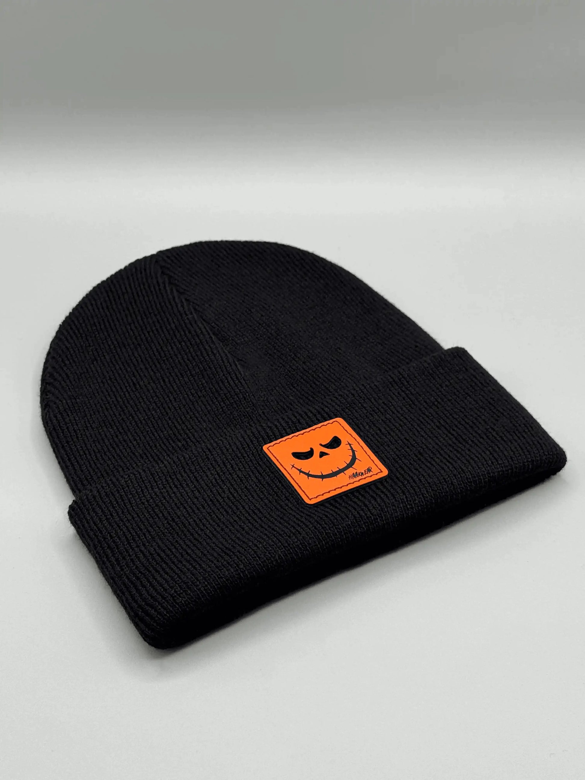 Black knit beanie with orange jack-o-lantern patch on front