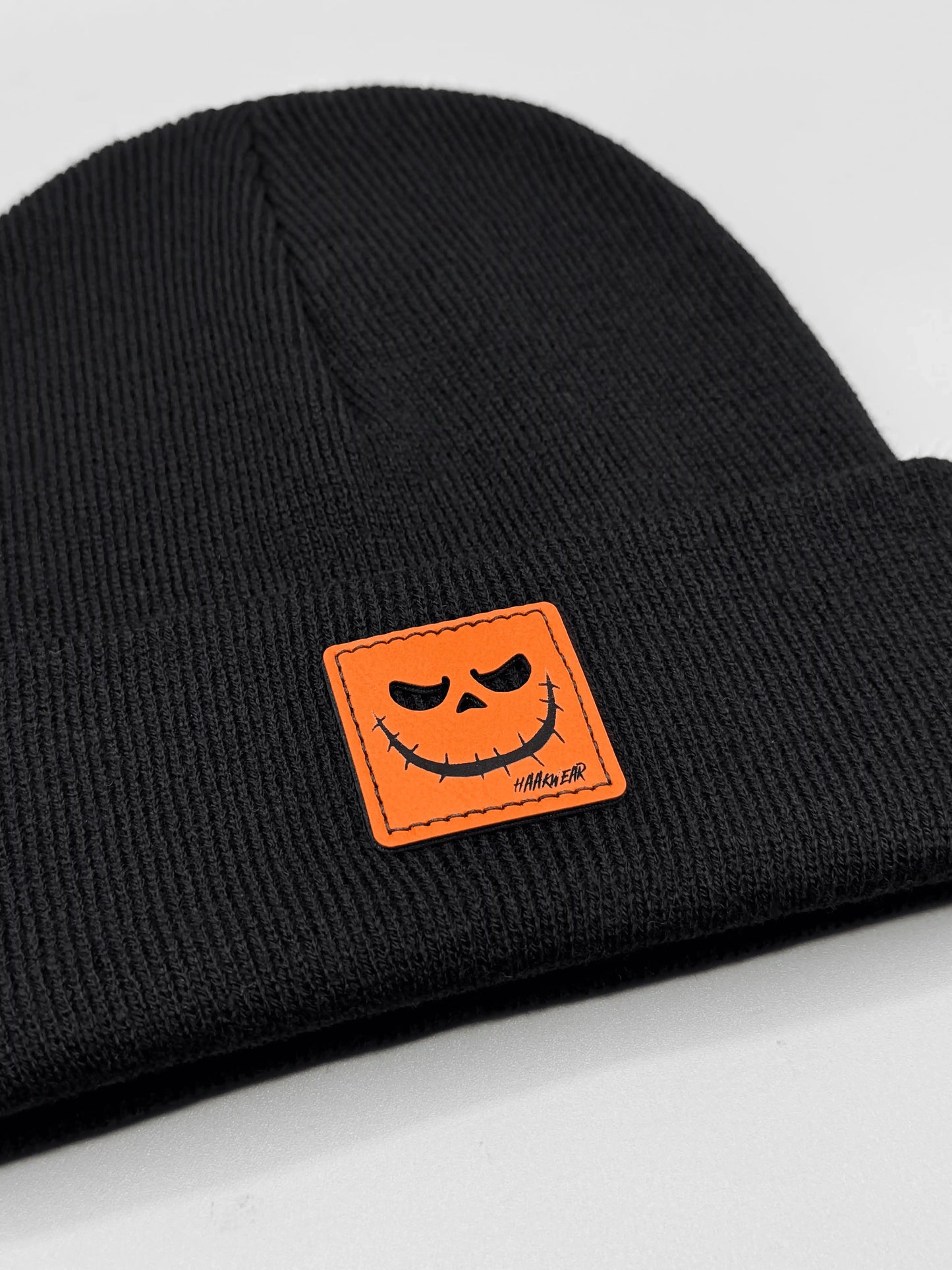 Dark knit beanie with orange jack-o-lantern patch centered on front