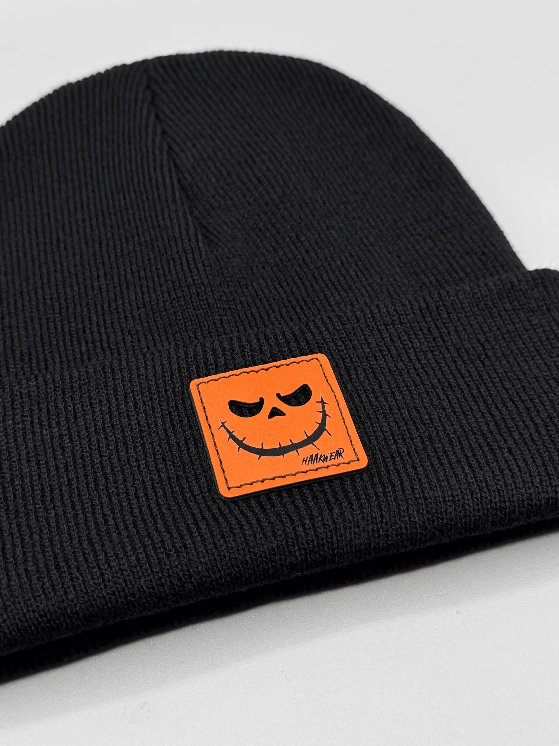 Dark knit beanie with orange jack-o-lantern patch centered on front