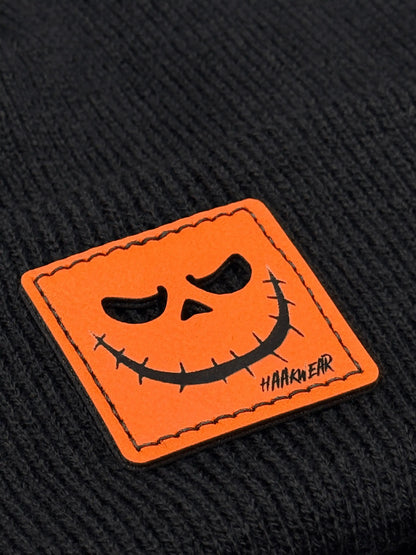 Orange jack-o-lantern face patch on dark knit beanie with stitched border