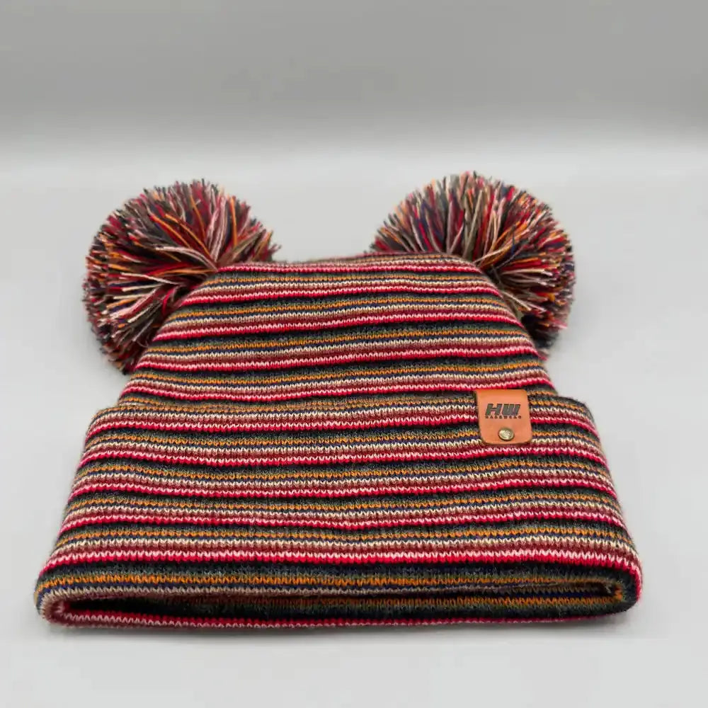 Folded knit beanie with multicolor stripes, two pom poms, and small front patch.