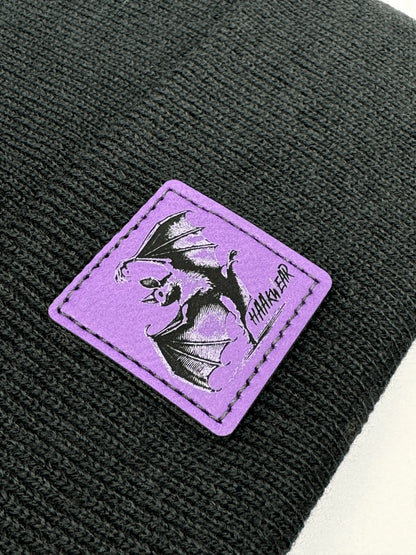 Dark navy knit beanie close-up: purple patch with witch and broom graphic