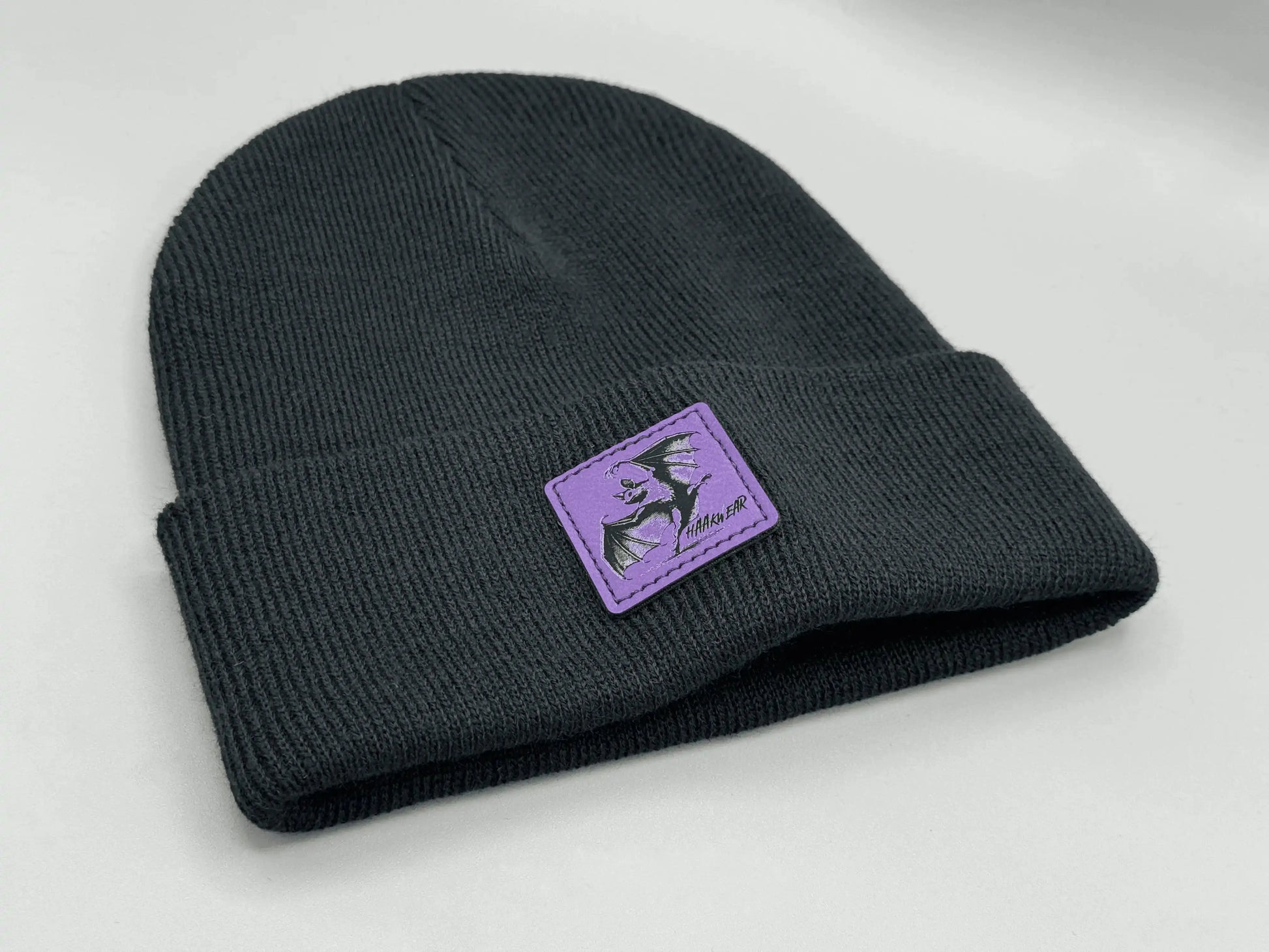 Dark navy knit beanie with purple square logo patch on the side