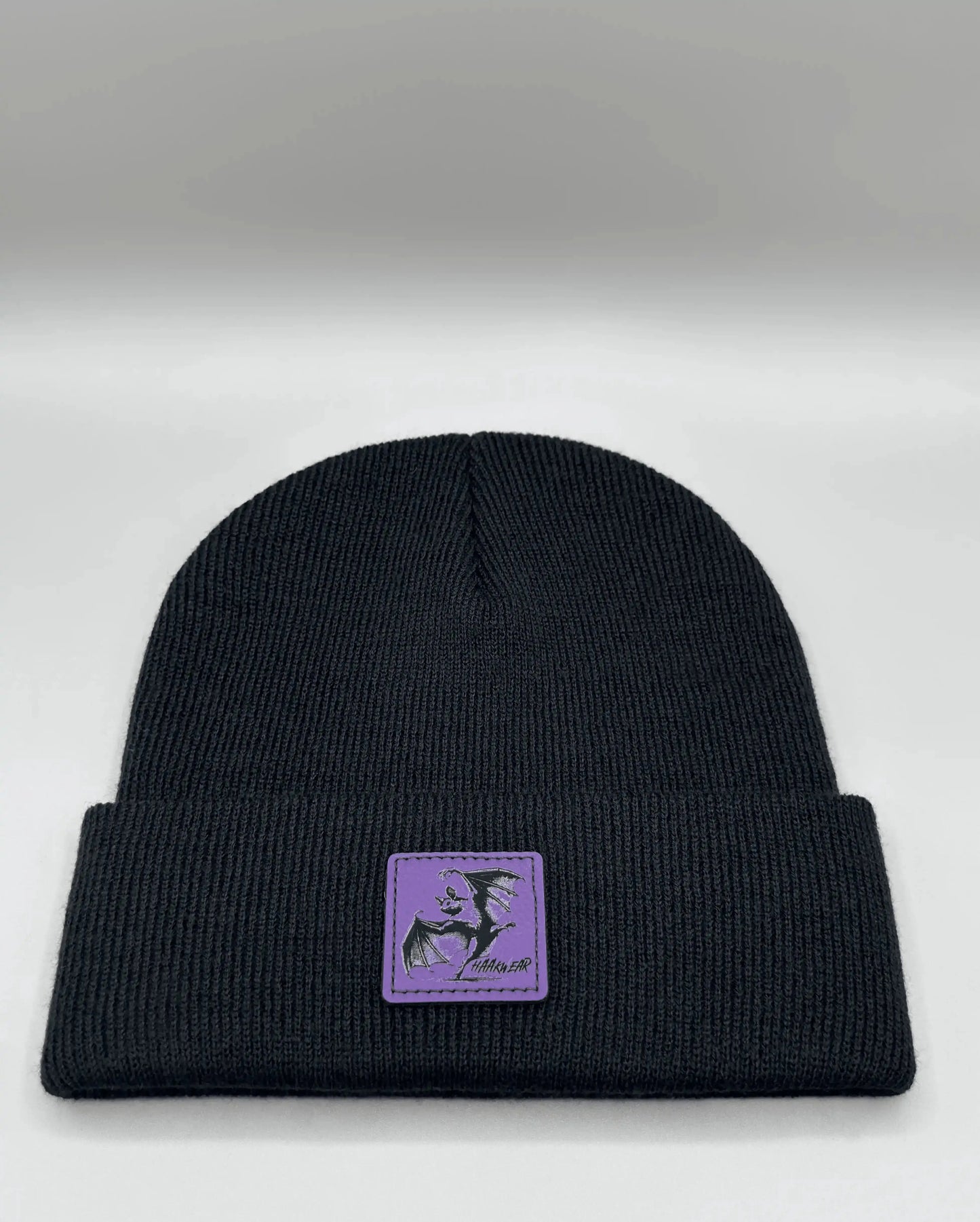 Dark navy knit beanie with small purple patch centered on the front
