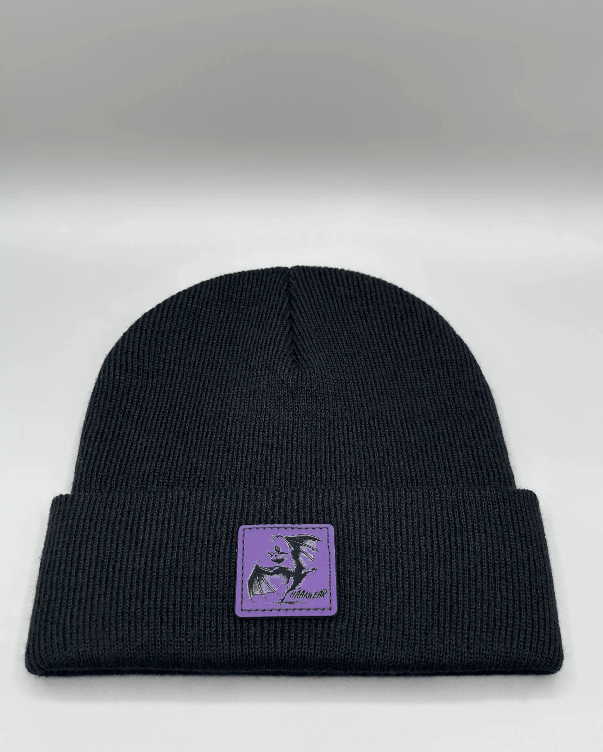 Dark navy knit beanie with small purple patch centered on the front