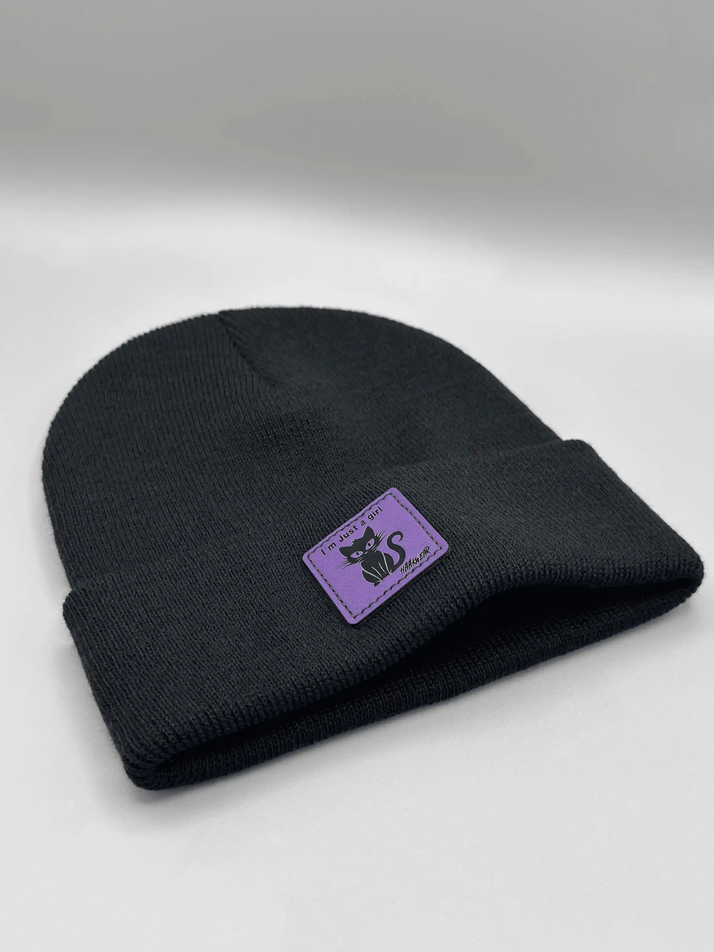 Black knit beanie folded cuff with small purple cat logo patch.