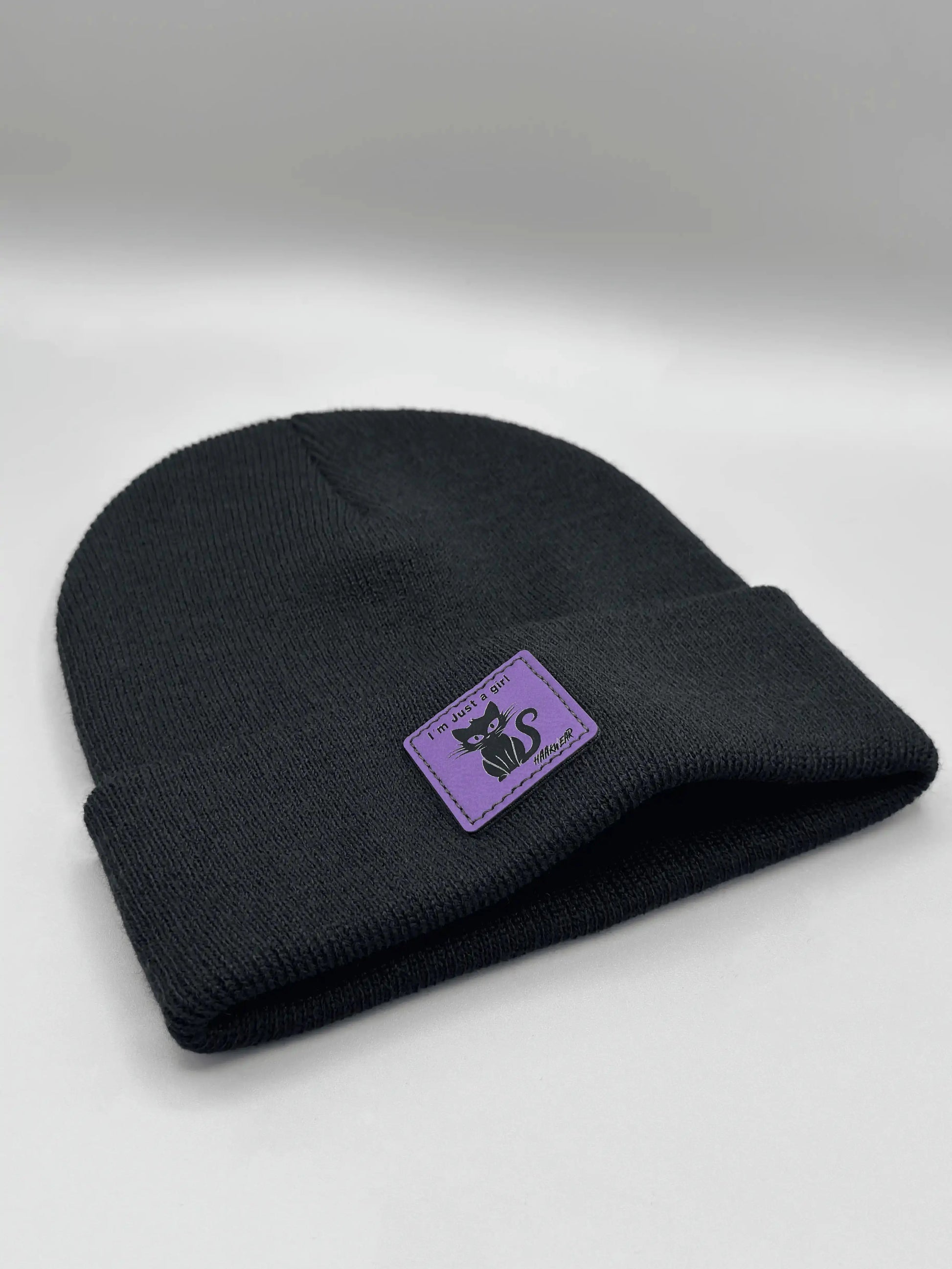 Black knit beanie folded cuff with small purple cat logo patch.