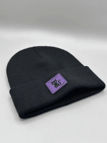 Black knit beanie folded cuff with small purple cat logo patch.