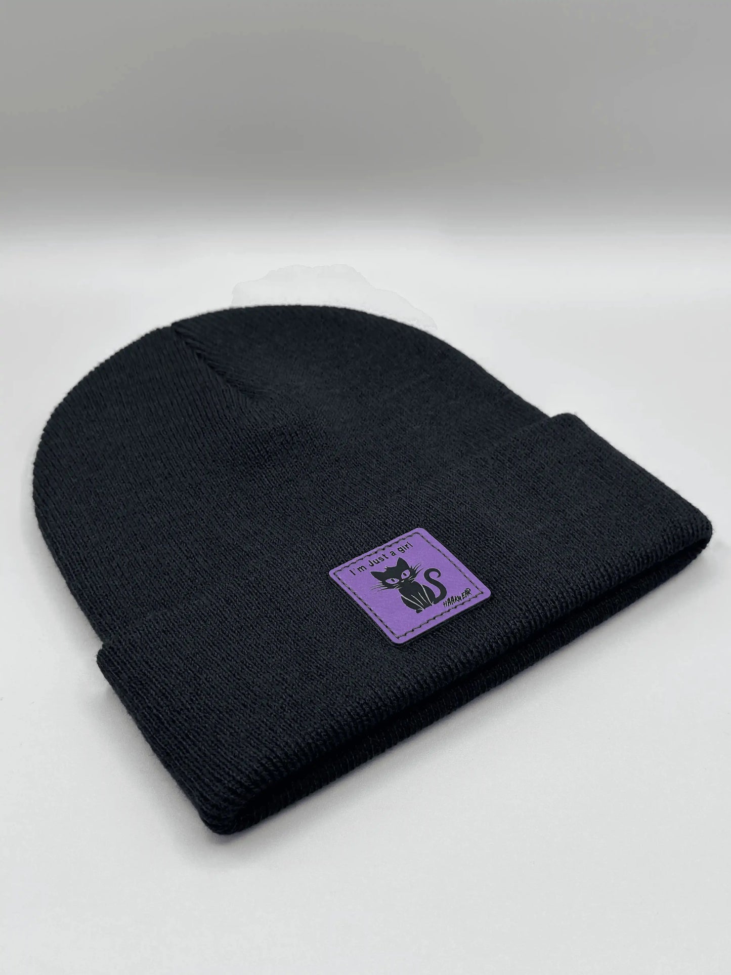 Black knit beanie with purple cat patch on the cuff side.