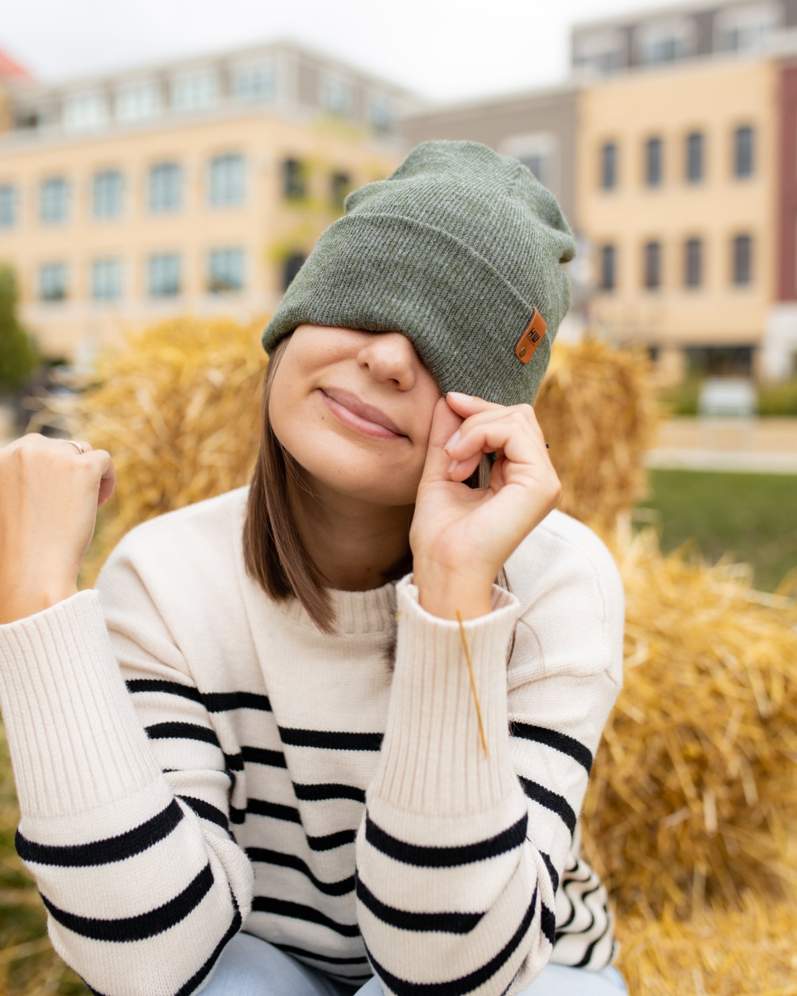 Person wearing a green beanie and striped sweater outdoors with buildings in the background