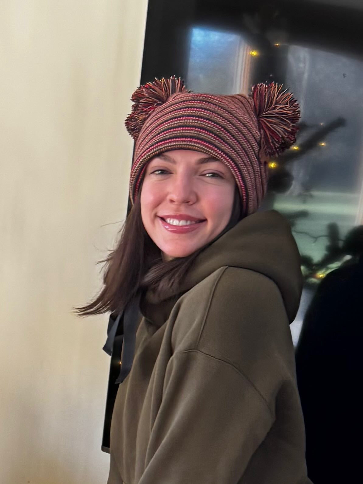 Person wearing a striped beanie with pom-poms in front of a vehicle.