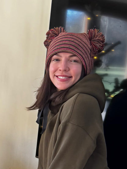 Person wearing a striped beanie with pom-poms in front of a vehicle.