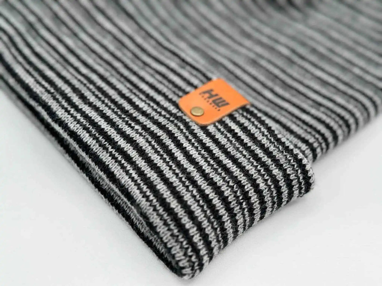 Black-and-gray striped ribbed beanie with folded cuff, woven tag on front