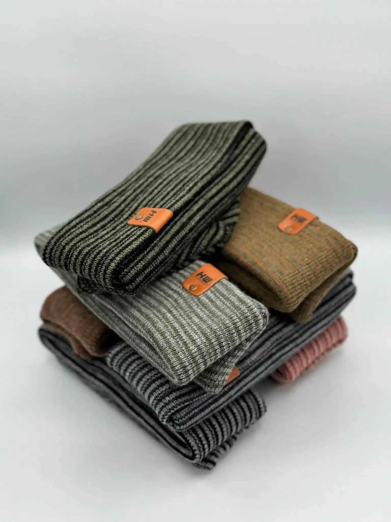 Stack of striped knit beanies with fold-over cuffs and orange logo patches
