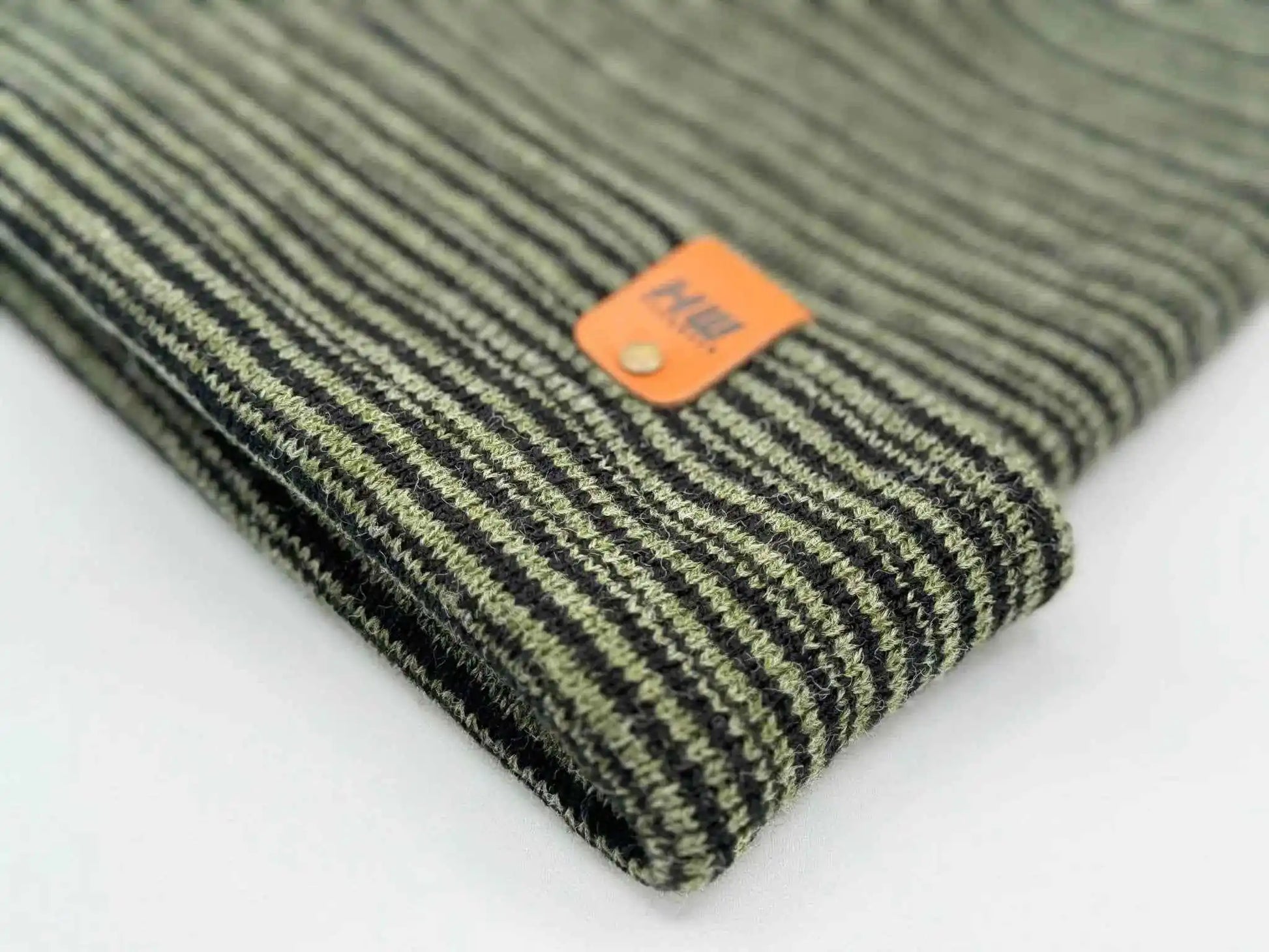 Knit beanie cuff corner with orange logo patch and dark green striped texture