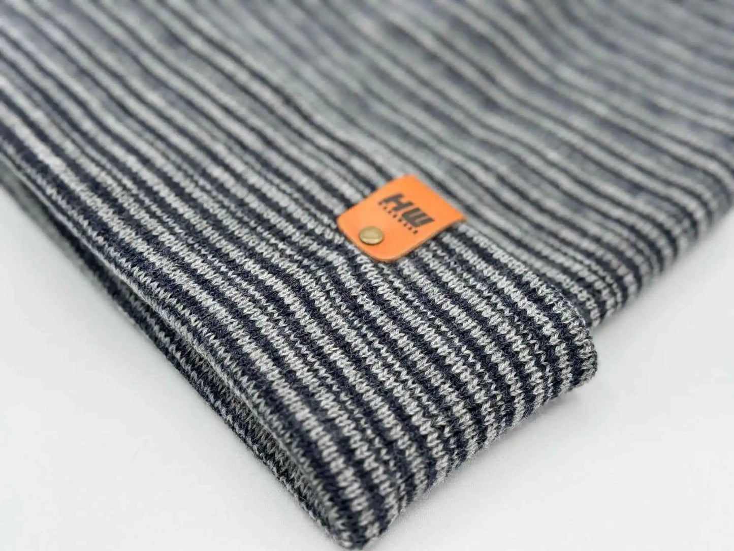 Striped knit cuffed beanie close-up with orange logo patch, gray and navy tones