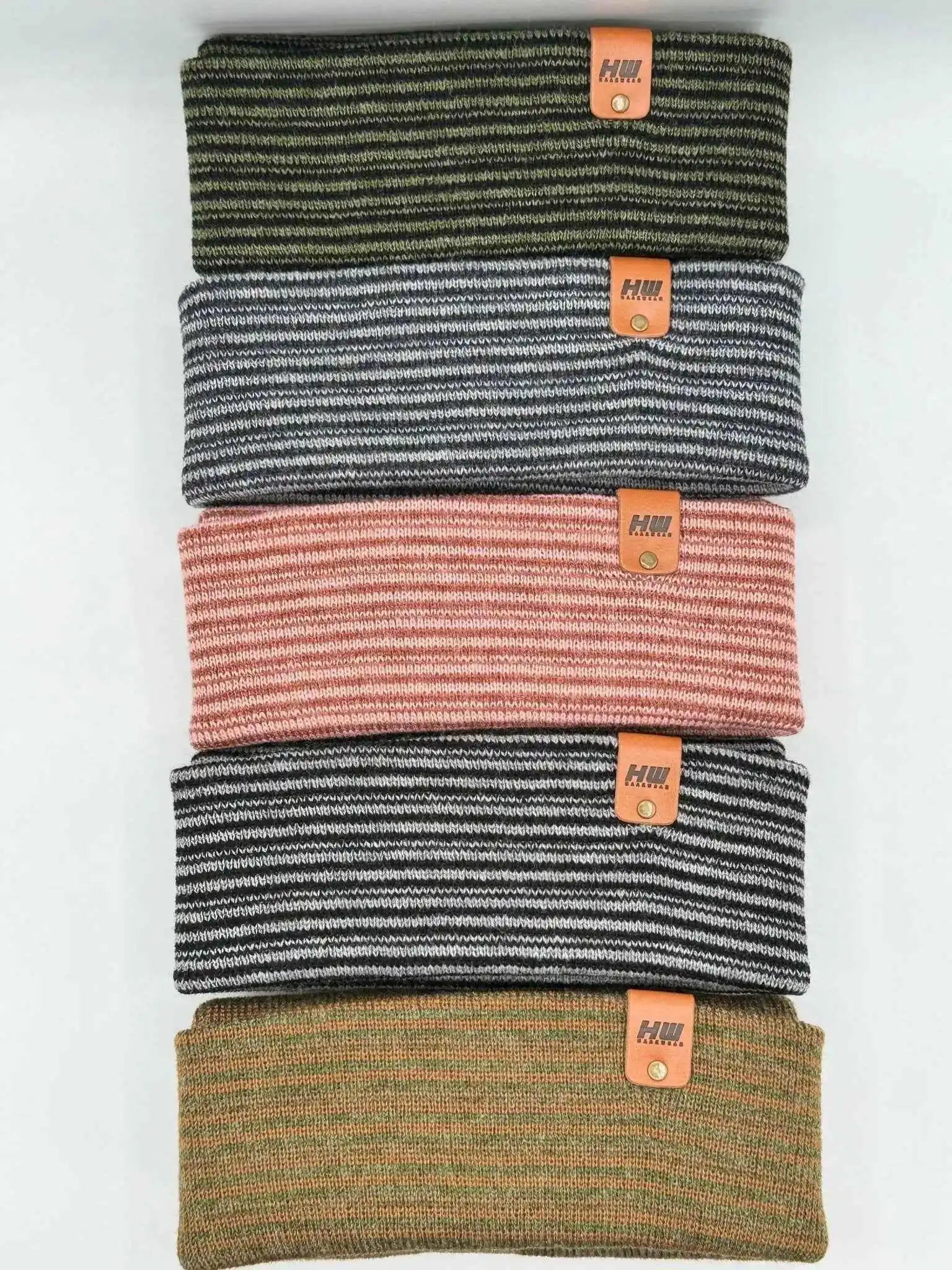 Stack of cuffed beanies in gray/navy, pink, and olive with orange logo patches